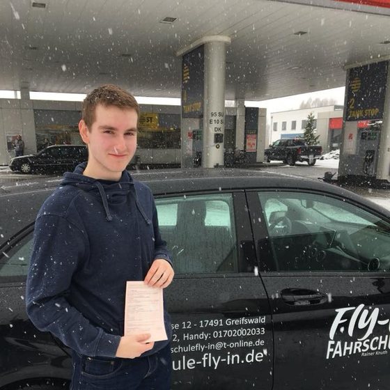 Fahrschülerin mit bestandener Prüfbescheinigung vor dem Fahrschulwagen
