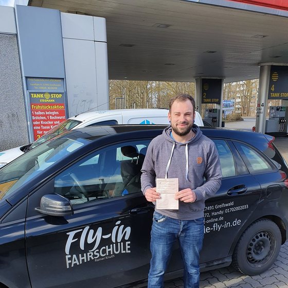 Fahrschüler nach bestandener Prüfung vor dem Fahrschulwagen